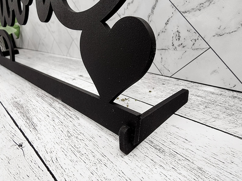 May include: Black metal sign with the word "Love" in a stylized font. The sign has a heart shape at the top and a flat base.