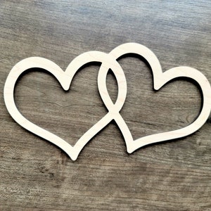 May include: Two wooden hearts intertwined, creating a symbol of love and unity. The hearts are cut from a light brown wood and are displayed against a dark brown wooden background.