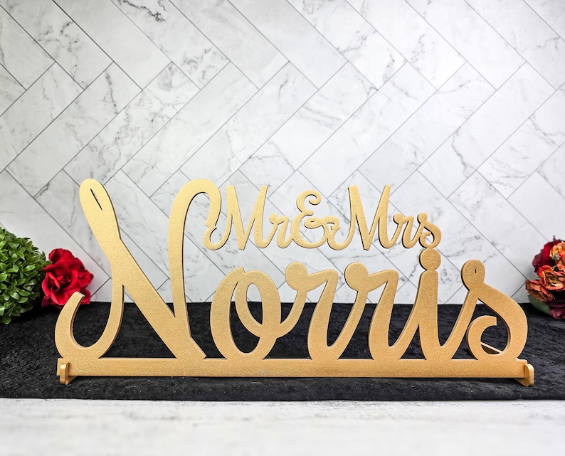 May include: Gold-colored wooden sign with the text "Mr. & Mrs. Norris" in a cursive font. The sign is perfect for a wedding or anniversary celebration.