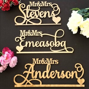 Op de afbeelding: Drie houten borden met de tekst "Mr. & Mrs. Stevens", "Mr. & Mrs. Emeasobu" en "Mr. & Mrs. Anderson" in een cursief schrift. Elk bord heeft een klein hartvormig uitsnijding.