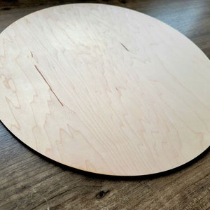 May include: A round, unfinished, light wood circle with a smooth surface. The circle is made of maple wood and has a natural grain pattern.