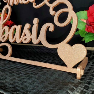 Op de afbeelding: Een houten bord met de woorden "Mr. & Mrs. Kobasic" in cursief schrift. Het bord is in een lichtbruine kleur geverfd en heeft een glitterafwerking. Een klein hartvormig uitsnijding is aan het bord bevestigd.