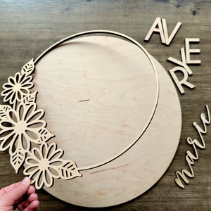 May include: A wooden craft kit for creating a personalized wreath. The kit includes a wooden circle with a cutout design, a floral design, and the words "AVRYE marie".