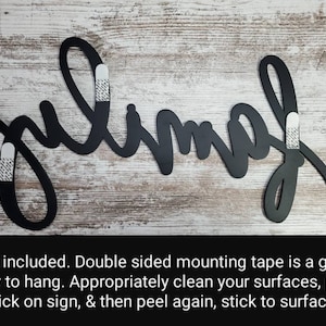 May include: Black metal wall decor with the word "julimah" written in a cursive script. The decor is attached to a white wood background with double-sided mounting tape.
