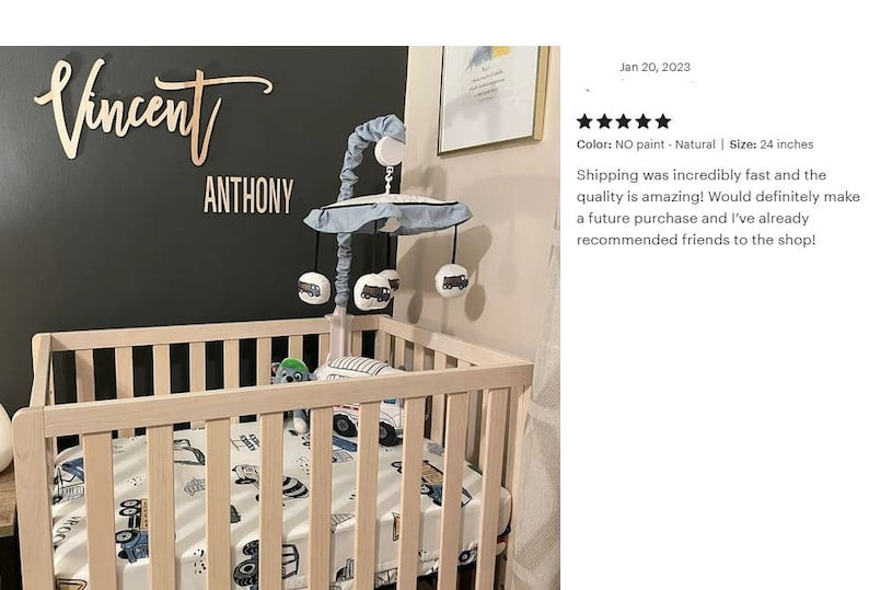 May include: A wooden crib with a white and blue truck themed bedding set. A wooden mobile with blue fabric and truck-shaped toys hangs above the crib. The crib is in front of a dark gray wall with a wooden sign that reads "Vincent" and "Anthony".