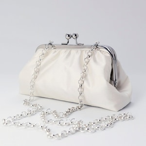 May include: A white satin clutch bag with a silver chain strap and a silver clasp.