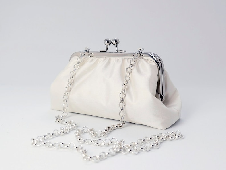 May include: A white satin clutch bag with a silver chain strap and a silver clasp.