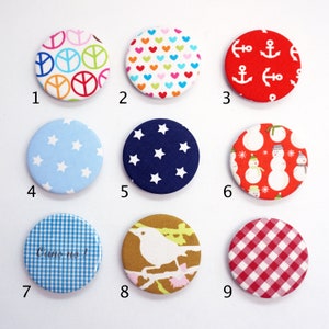 Könnte beinhalten: Neun runde Stoffknöpfe mit verschiedenen Designs. Die Knöpfe sind von 1 bis 9 nummeriert. Die Designs umfassen Friedenszeichen, Herzen, Anker, Sterne, Schneemänner, Gingham und einen Vogel auf einem Ast.