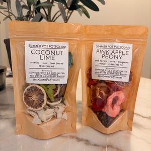 May include: Two stand-up pouches of simmer pot potpourri. The left pouch is labeled Coconut Lime with dried lime slices and coconut flakes. The right pouch is labeled Pink Apple Peony with dried apple slices and red petals. Both include directions.