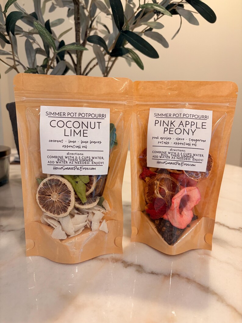 May include: Two stand-up pouches of simmer pot potpourri. The left pouch is labeled Coconut Lime with dried lime slices and coconut flakes. The right pouch is labeled Pink Apple Peony with dried apple slices and red petals. Both include directions.