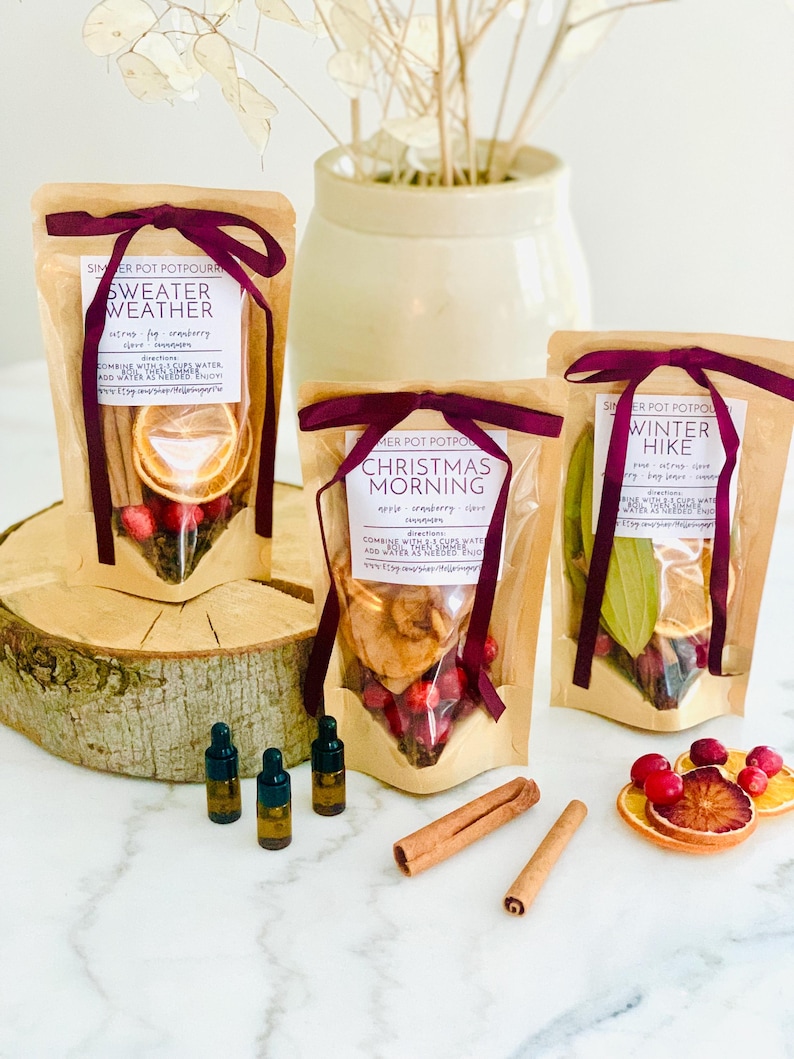 May include: Three kraft paper pouches of simmer pot potpourri labeled Sweater Weather, Christmas Morning, and Winter Hike, each tied with a dark purple ribbon. Includes three small amber glass dropper bottles and two cinnamon sticks.