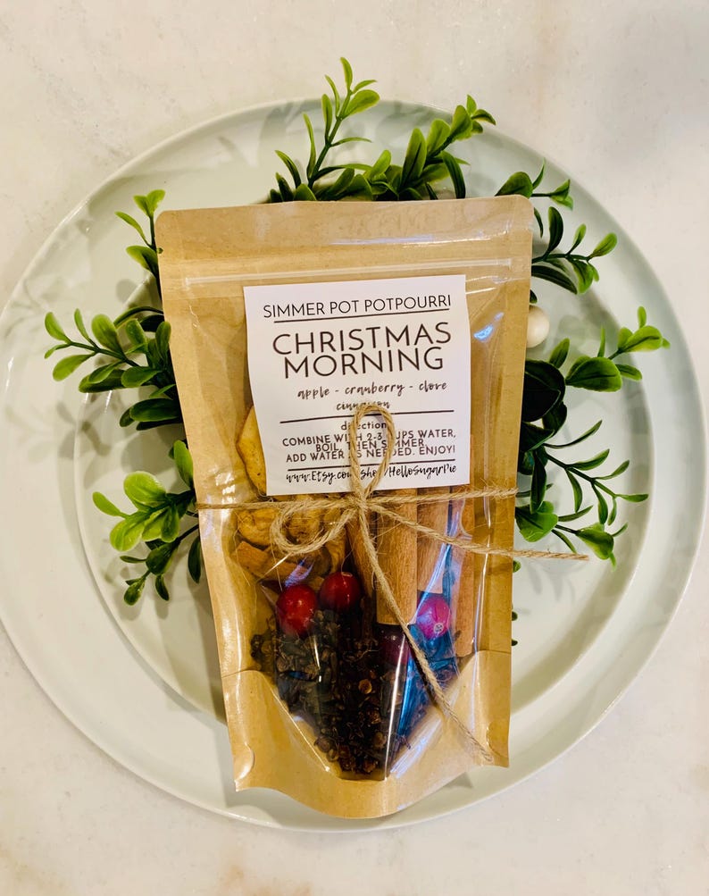May include: A clear pouch of Christmas Morning simmer pot potpourri featuring dried apple slices, red cranberries, whole cloves, and cinnamon sticks. The label includes directions to combine with 2-3 cups of water and simmer.