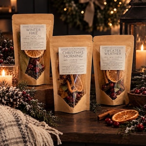 May include: Three brown paper pouches of simmer pot potpourri labeled Winter Hike, Christmas Morning, and Sweater Weather. Each pouch features a clear window displaying dried orange slices, cranberries, and spices. The labels include instructions to combine with 2-3 cups of water and simmer.