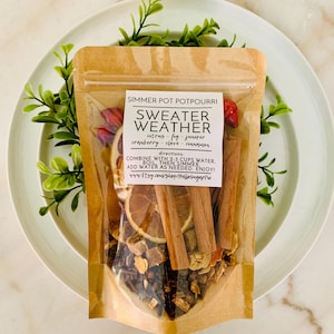 May include: A clear and brown pouch of Sweater Weather simmer pot potpourri containing dried orange slices, cinnamon sticks, and spices. The label lists ingredients including citrus, fig, juniper, cranberry, clove, and cinnamon with instructions.