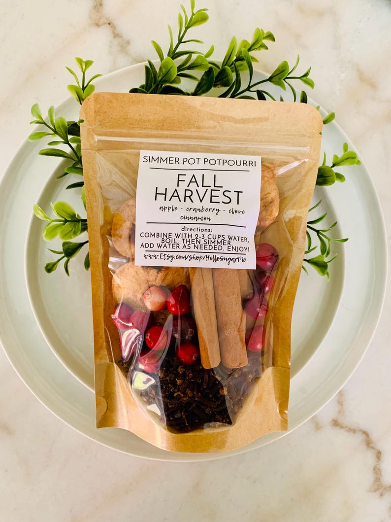 May include: A clear and brown pouch of Fall Harvest simmer pot potpourri containing dried apple slices, red cranberries, cinnamon sticks, and cloves. The label reads: SIMMER POT POTPOURRI, FALL HARVEST, apple, cranberry, clove, cinnamon, directions.