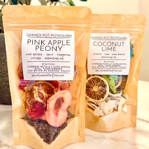 May include: Two kraft paper pouches of simmer pot potpourri. One is labeled "Pink Apple Peony" with pink apple slices, cloves, and petals. The other is "Coconut Lime" with coconut flakes and lime slices. Both include instructions and the Etsy shop URL.