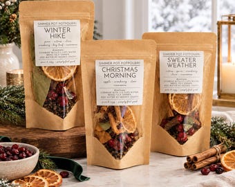 May include: Three brown kraft paper pouches of simmer pot potpourri labeled Winter Hike, Christmas Morning, and Sweater Weather. Each pouch features a clear window displaying dried orange slices, cranberries, and spices with printed instructions.