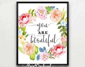 May include: A watercolor print with a floral wreath of pink, peach, and blue flowers. The text "you are beautiful" is written in black cursive lettering in the center of the wreath.