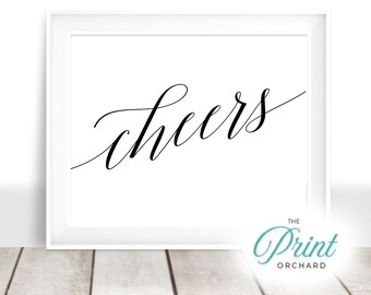 May include: A white framed print with the word "cheers" written in black cursive script. The print is on a white background and has a subtle, elegant design.