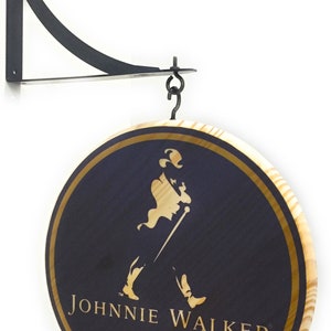 May include: A round wooden sign with a gold border and a black background. The sign features the Johnnie Walker logo, which includes a man in a top hat walking with a cane. The sign is hanging from a black metal bracket.