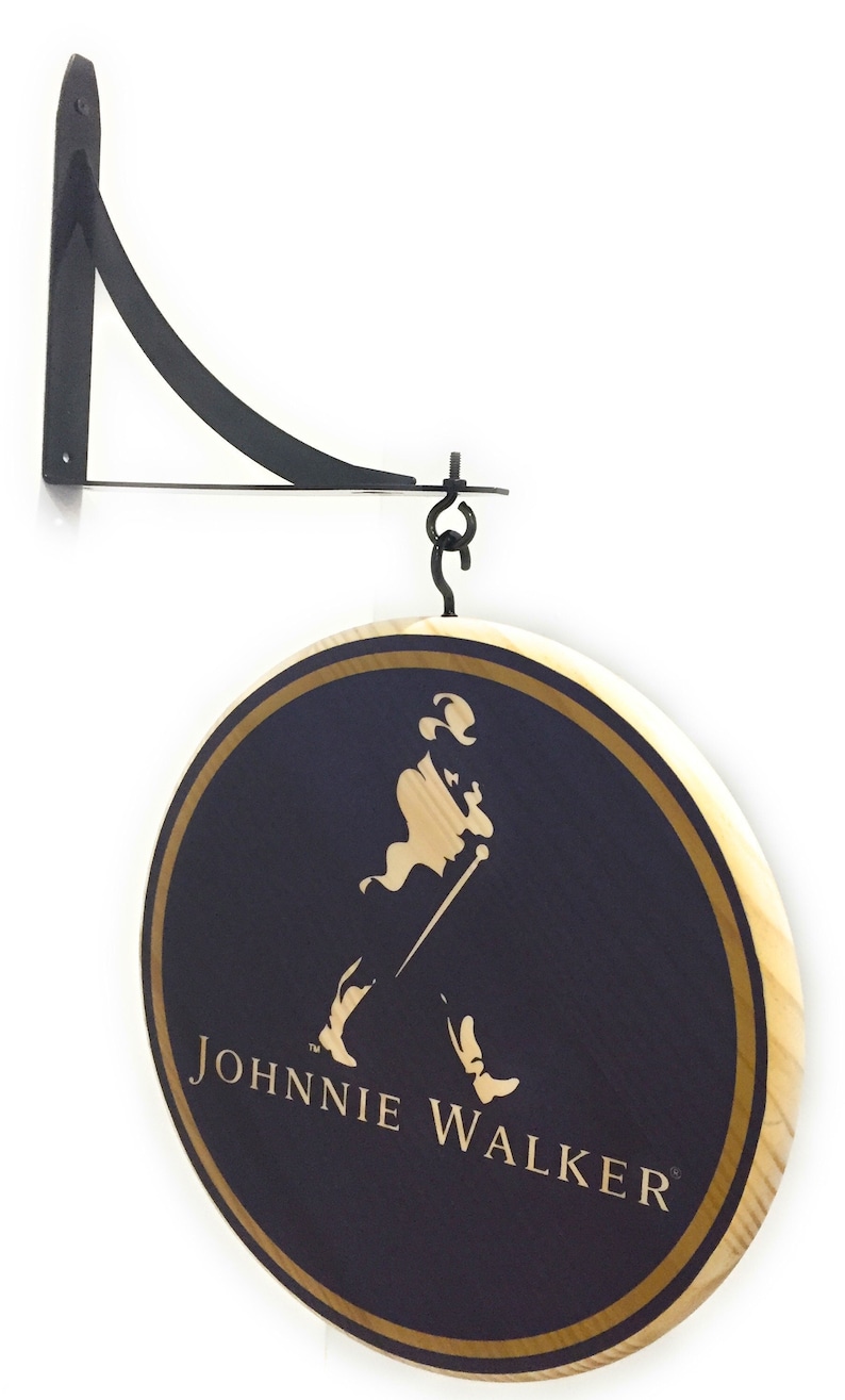May include: A round wooden sign with a gold border and a black background. The sign features the Johnnie Walker logo, which includes a man in a top hat walking with a cane. The text "JOHNNIE WALKER" is written in gold letters below the logo.