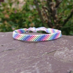 May include: A rainbow friendship bracelet made with colourful embroidery floss. The bracelet is woven in a chevron pattern and has a simple knot closure.