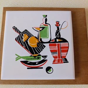 May include: A decorative tile with a retro still life design. The image features a cutting board, bottles, a fish, and a cocktail glass. The colour palette includes black, red, green, yellow, and white. The tile is set in a wooden frame.