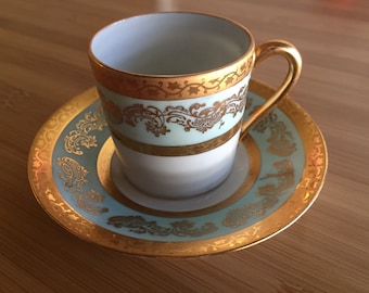 Może przedstawiać: Zestaw filiżanki i spodeczka do herbaty z białej porcelany z pozłacanym rantem i misternymi kwiatowymi wzorami w kolorze niebieskim i złotym.