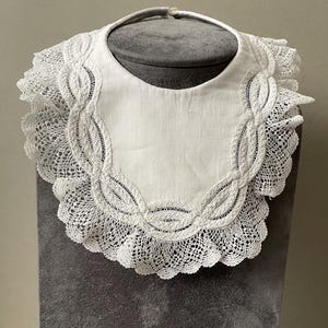 Antique baby&#39;s bib with lace edging in white.