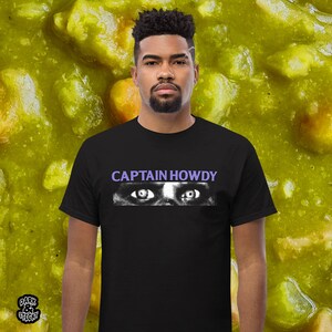 May include: A black t-shirt with a white graphic of a pair of eyes and the text "CAPTAIN HOWDY" in purple.