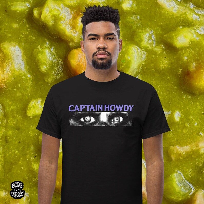 May include: A black t-shirt with a white graphic of a pair of eyes and the text "CAPTAIN HOWDY" in purple.