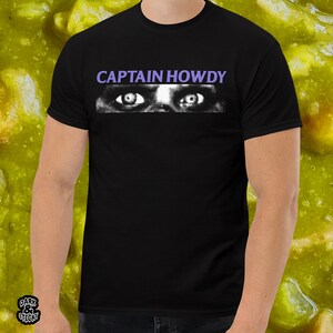 May include: Black t-shirt with the text "CAPTAIN HOWDY" in white letters and a graphic of two eyes with purple eyelids.