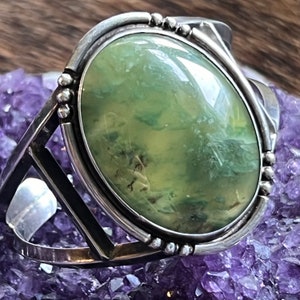 May include: A silver cuff bracelet featuring a large oval green stone set in the centre. The stone has a mottled green and yellow pattern.