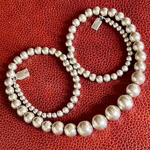 May include: A silver beaded necklace with two strands of varying sizes. The necklace is made of round beads and has a clasp closure.