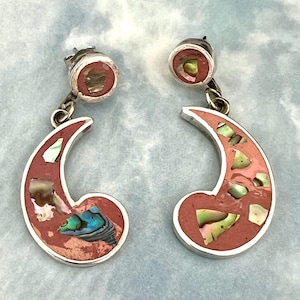 May include: A pair of sterling silver earrings with a crescent moon design. The earrings feature a red-orange inlay with iridescent abalone shell accents. The earrings have a post-back closure.