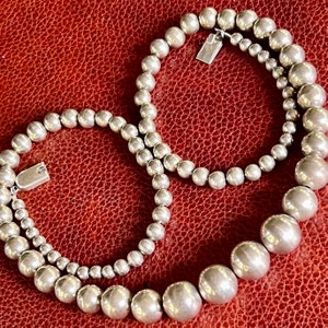 May include: Two silver necklaces with round beads. The necklace on top has smaller beads and the necklace on the bottom has larger beads.