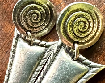 May include: Silver earrings with a triangular shape and a spiral design. The earrings have a textured edge.