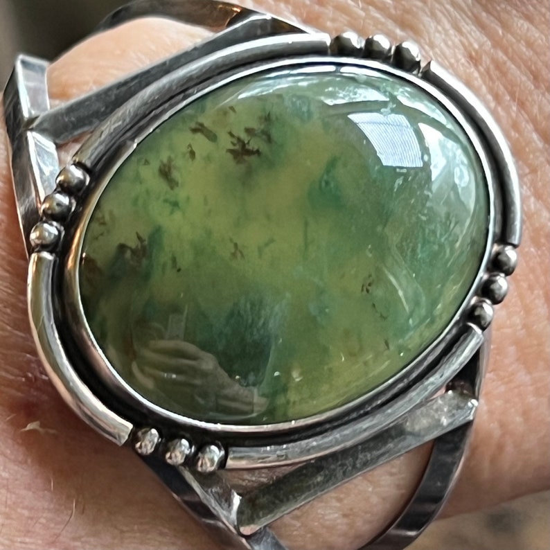 May include: A silver ring featuring a green agate stone set in a bezel setting. The stone displays a mottled green and brown pattern.