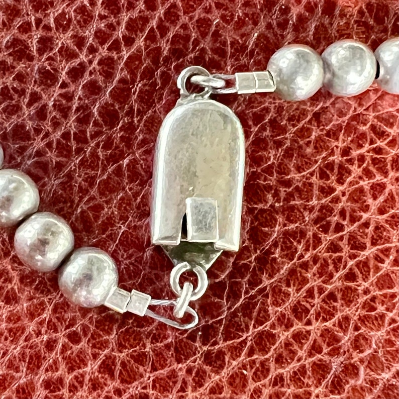 May include: A silver clasp with a rounded, rectangular shape, attached to a silver chain with round beads.