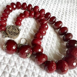May include: A red gemstone necklace with a silver clasp and matching earrings. The necklace is made of large, faceted beads.