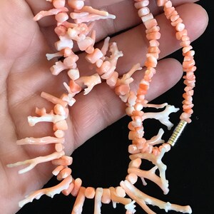 Op de afbeelding: Een roze koraal ketting met een zilveren sluiting. De ketting is gemaakt van kleine, onregelmatige stukjes koraal, waarvan sommige de vorm van takken hebben. De ketting is ongeveer 46 cm lang.