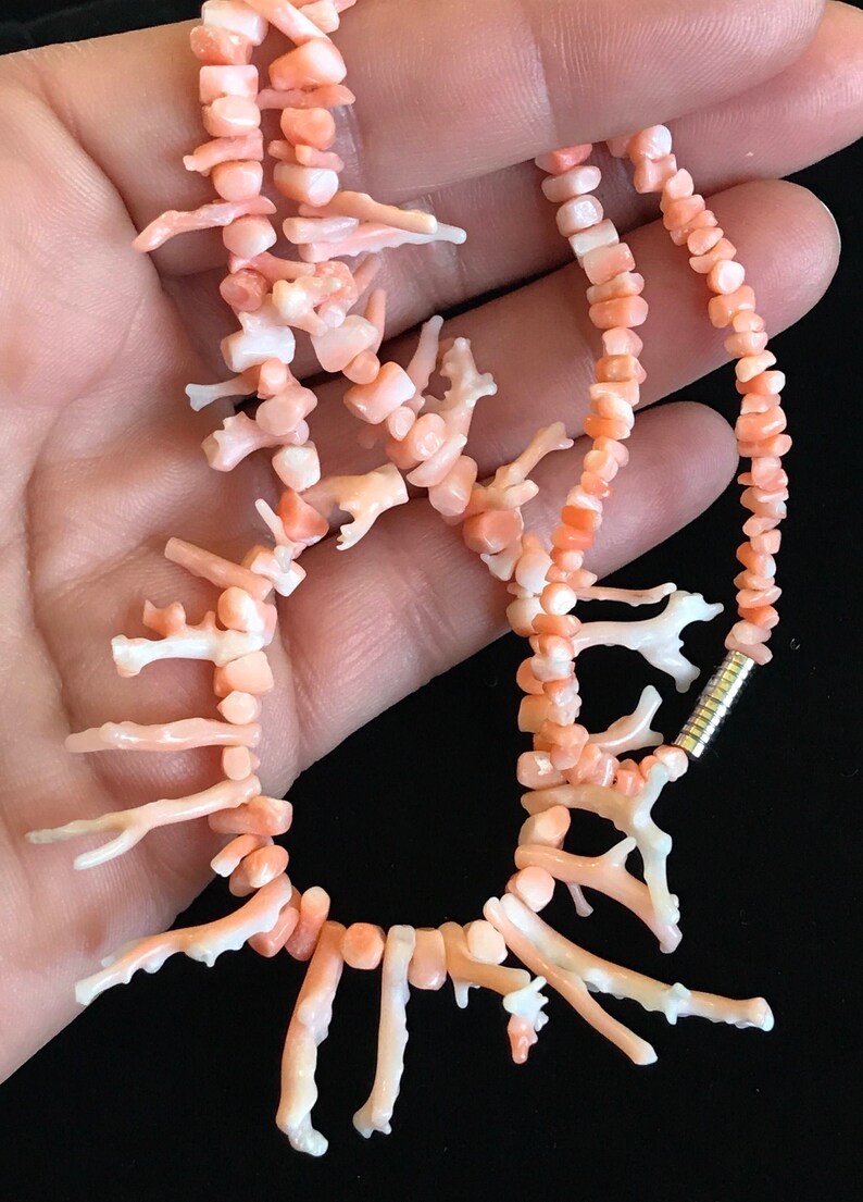 Op de afbeelding: Een roze koraal ketting met een zilveren sluiting. De ketting is gemaakt van kleine, onregelmatige stukjes koraal, waarvan sommige de vorm van takken hebben. De ketting is ongeveer 46 cm lang.