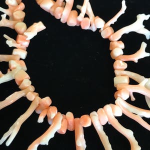 Op de afbeelding: Een ketting gemaakt van roze koraaltakken. De takken zijn in een cirkelvormige opstelling gerangschikt en verbonden door kleine, ronde kralen. De ketting is een prachtig voorbeeld van natuurlijke koraalsieraden.