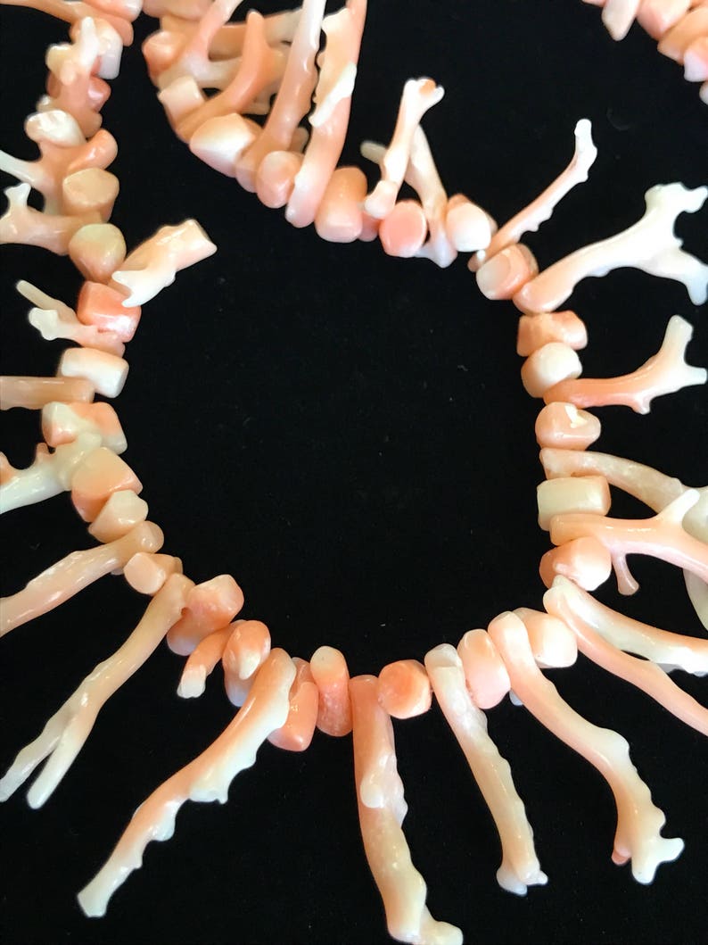Op de afbeelding: Een ketting gemaakt van roze koraaltakken. De takken zijn in een cirkelvormige opstelling gerangschikt en verbonden door kleine, ronde kralen. De ketting is een prachtig voorbeeld van natuurlijke koraalsieraden.