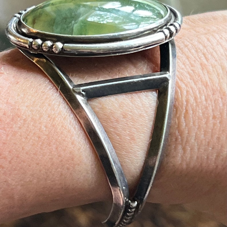 May include: A silver bracelet featuring a green stone cabochon set in a bezel. The bracelet has a triangular design with a single bar across the centre.