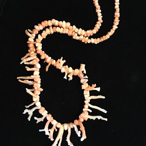 Op de afbeelding: Een roze koraal ketting met een lange streng kralen en een franje van koraaltakken.