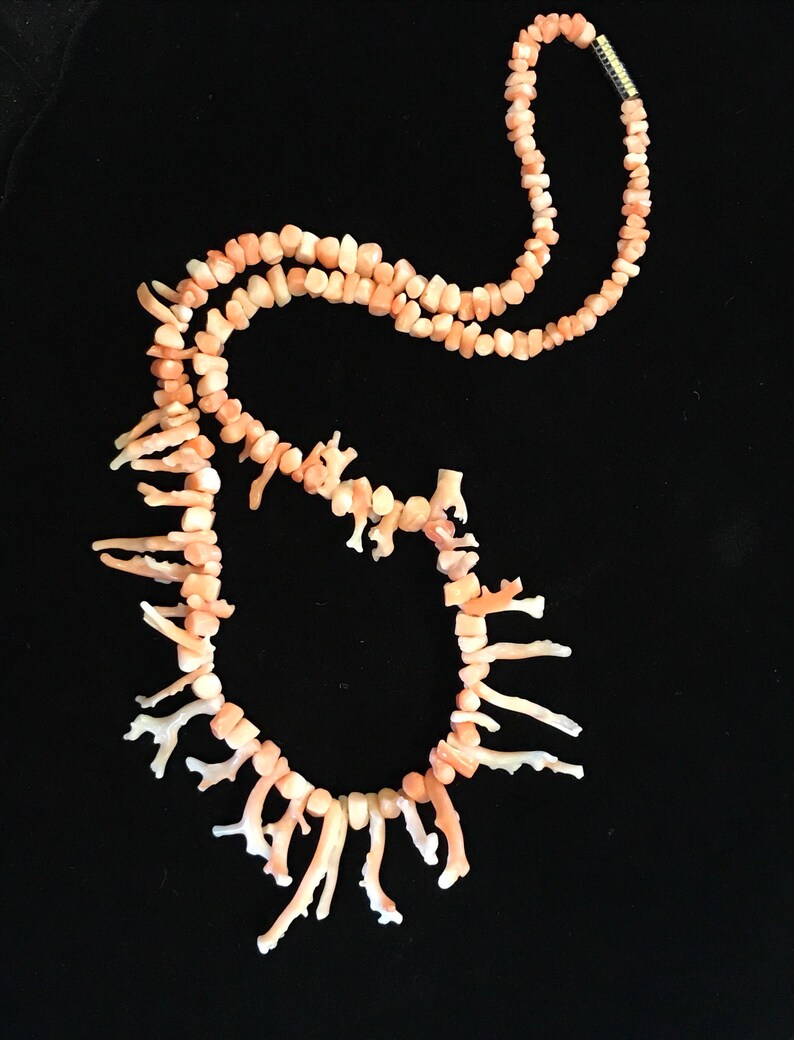 Op de afbeelding: Een roze koraal ketting met een lange streng kralen en een franje van koraaltakken.