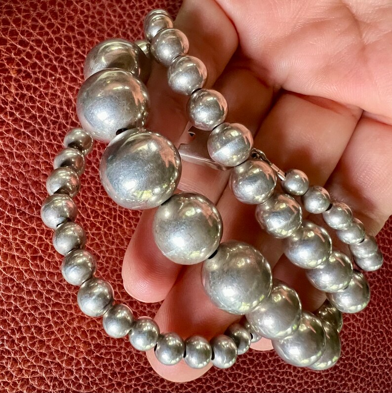 May include: A silver beaded necklace with large, round beads. The necklace is made of two strands of beads, with the larger beads on the top strand.