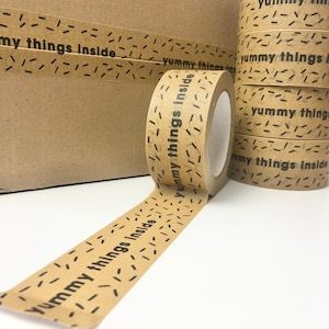 May include: A roll of brown packing tape with a repeating pattern of black dashes and the text "Yummy things inside" printed on it.