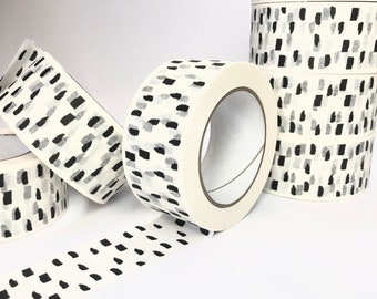 Puede incluir: Rollos de cinta washi blanca con un patrón abstracto negro y gris. La cinta está desenrollada y muestra el patrón.